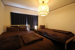 A room with two single beds, a bedside table with a lamp, and a hanging light fixture.