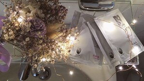 A glass table with a vase of dried flowers, a pair of glasses, and several packages of shampoo. - White House (Jinning)