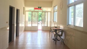 A hallway with a tiled floor, a door with a sign, and a window with a view of greenery. - White House (Jinning)