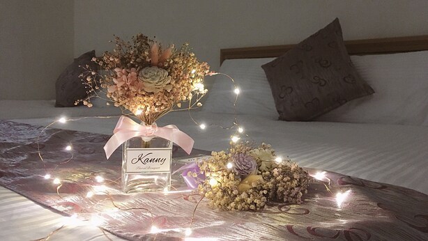 A bed with a floral arrangement and a bottle labeled "Kanny Floral Bouquet" on a patterned bedspread. - White House (Jinning)