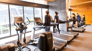A gym with treadmills and exercise equipment, large windows, and a modern interior design. - Madison Apartment (Melbourne)