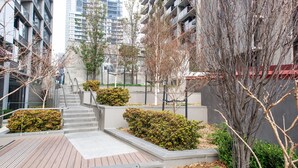 A modern urban courtyard with a wooden deck, concrete steps, and neatly trimmed bushes. - Madison Apartment (Melbourne)