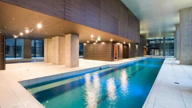 An indoor swimming pool with a modern design, surrounded by a large, curved wall structure. - Madison Apartment (Melbourne)