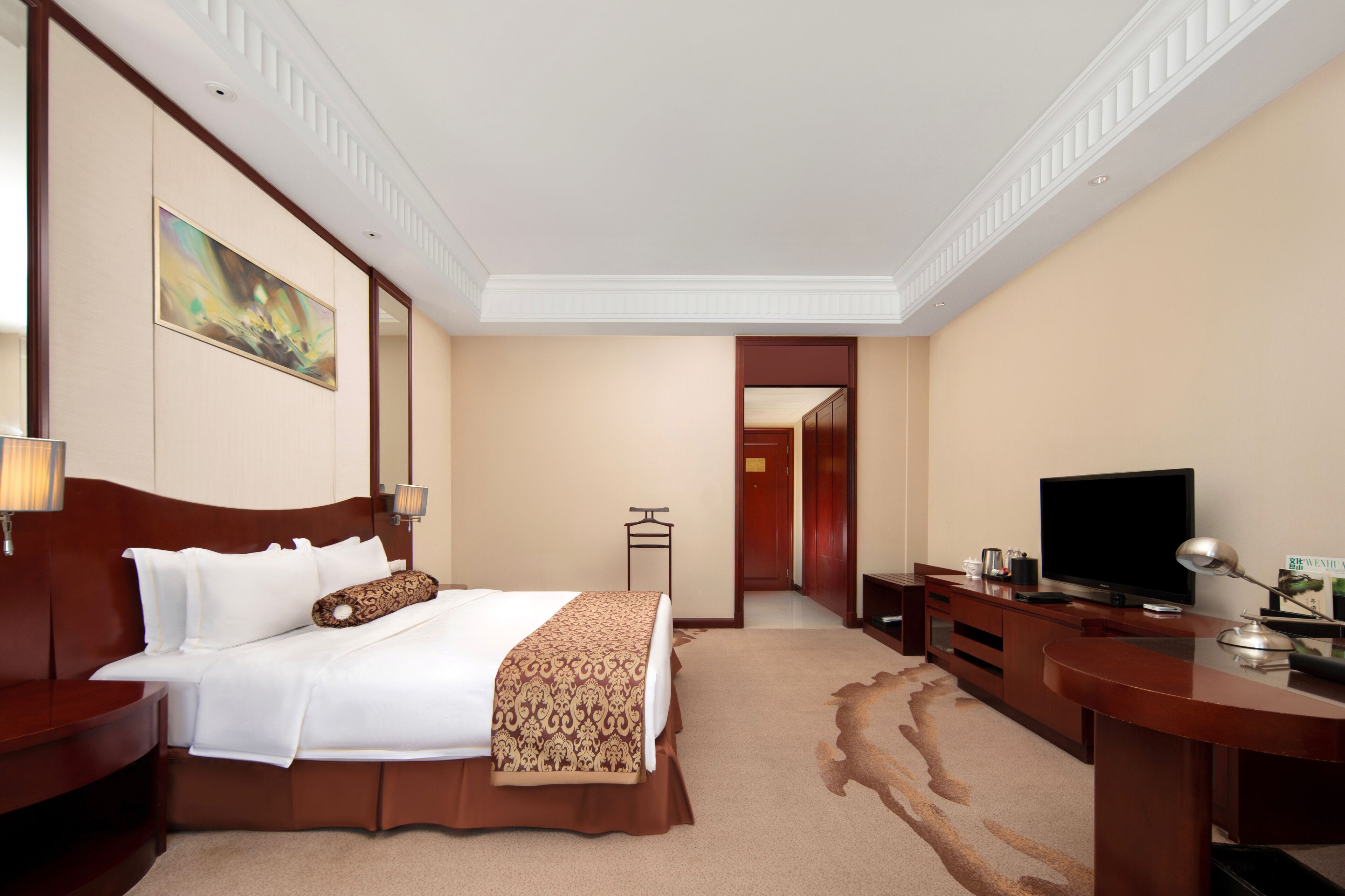 A hotel room with a large bed, a desk with a television, and a painting on the wall.