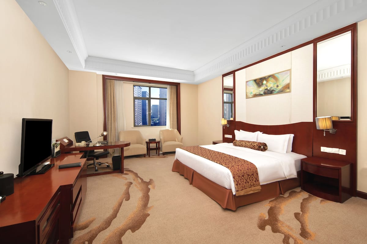 Ein Hotelzimmer mit einem großen Bett, einem Schreibtisch mit Computer, einem Fernseher und Blick auf die Stadt durch das Fenster.