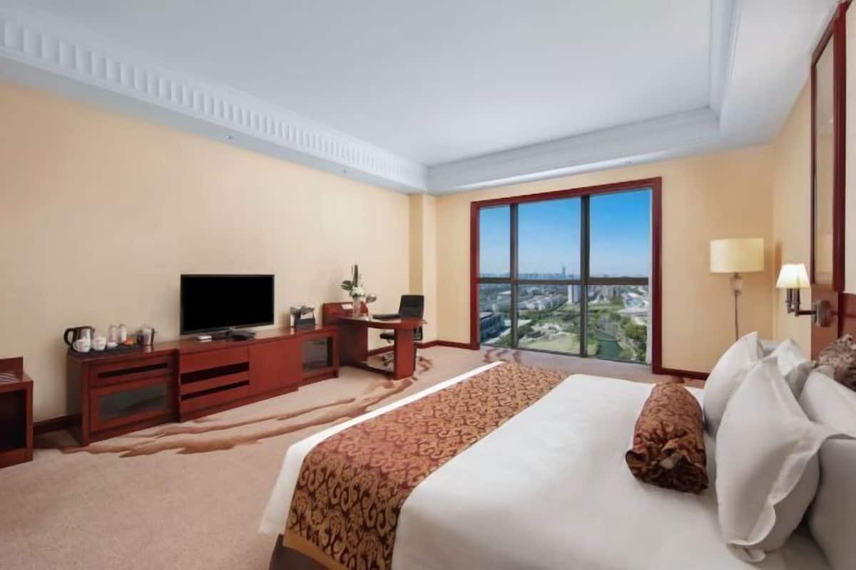 Ein Hotelzimmer mit einem großen Bett, einem Schreibtisch, einem Fernseher und Blick auf die Stadt.