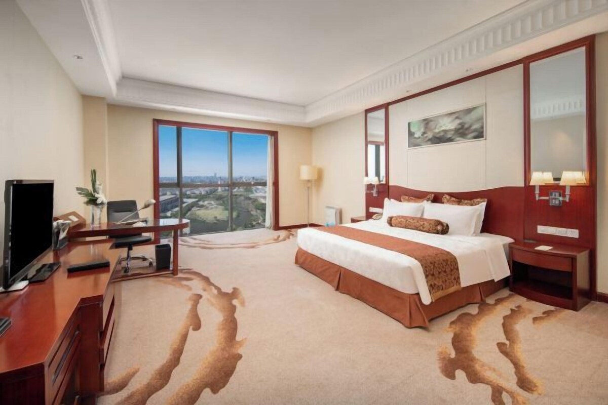 Una camera d'albergo con un letto grande, una scrivania con un computer, una televisione e vista sulla città.