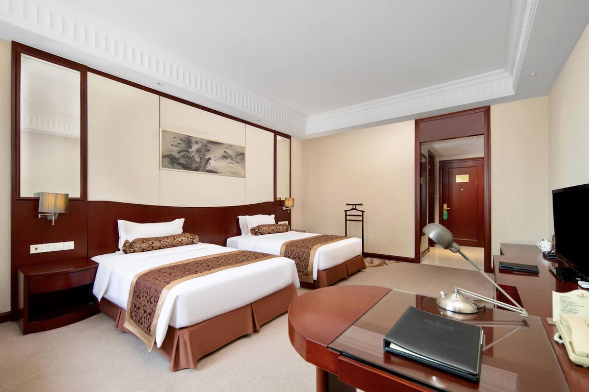 Ein Hotelzimmer mit zwei Betten, einem Schreibtisch, einem Fernseher und einem Bild an der Wand.