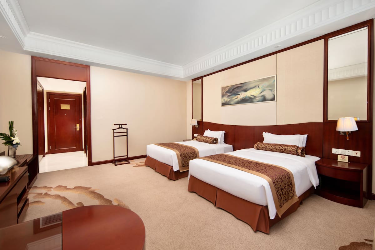 Ein Hotelzimmer mit zwei Betten, einem Schreibtisch, einem Sessel, einer Lampe und einem Bild an der Wand.