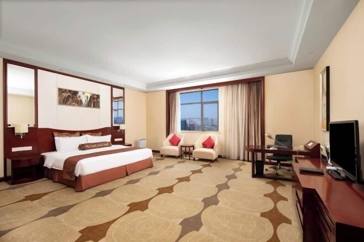 Ein Hotelzimmer mit einem großen Bett, einem Schreibtisch, einem Fernseher und einem Fenster mit Vorhängen.