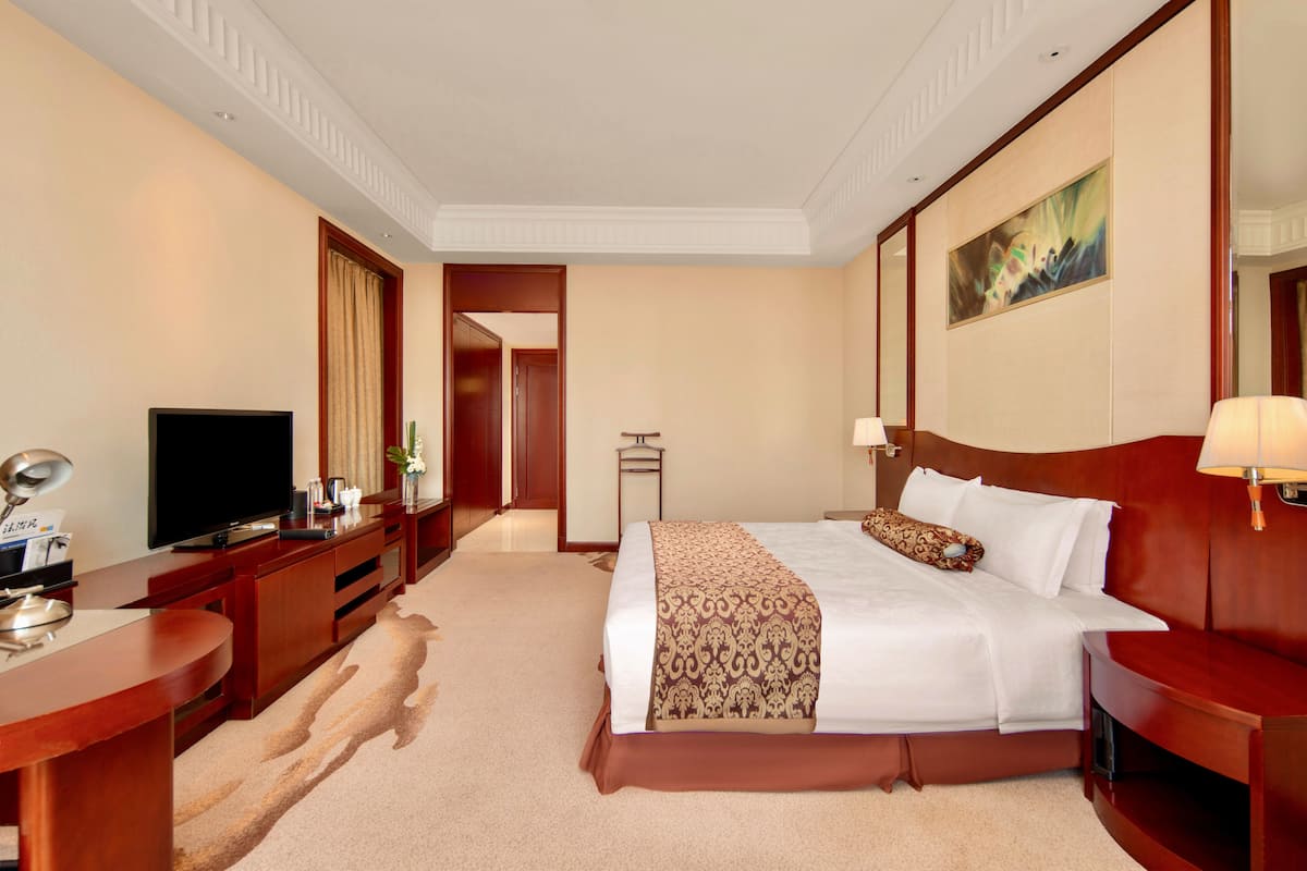 Ein Hotelzimmer mit einem großen Bett, einem Fernseher, einem Schreibtisch mit Lampe und einem Bild an der Wand.