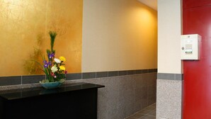 A reception area with a black counter, a flower arrangement, a red door, and a wall-mounted control panel. - Kyomai Inn (Kyoto)