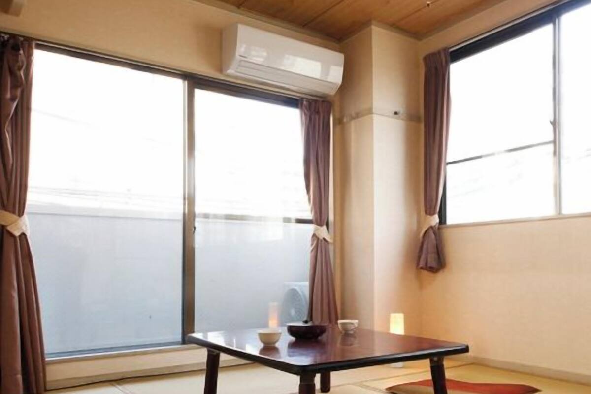 A room with tatami flooring, a low table with a bowl and a cup, and large windows with curtains.