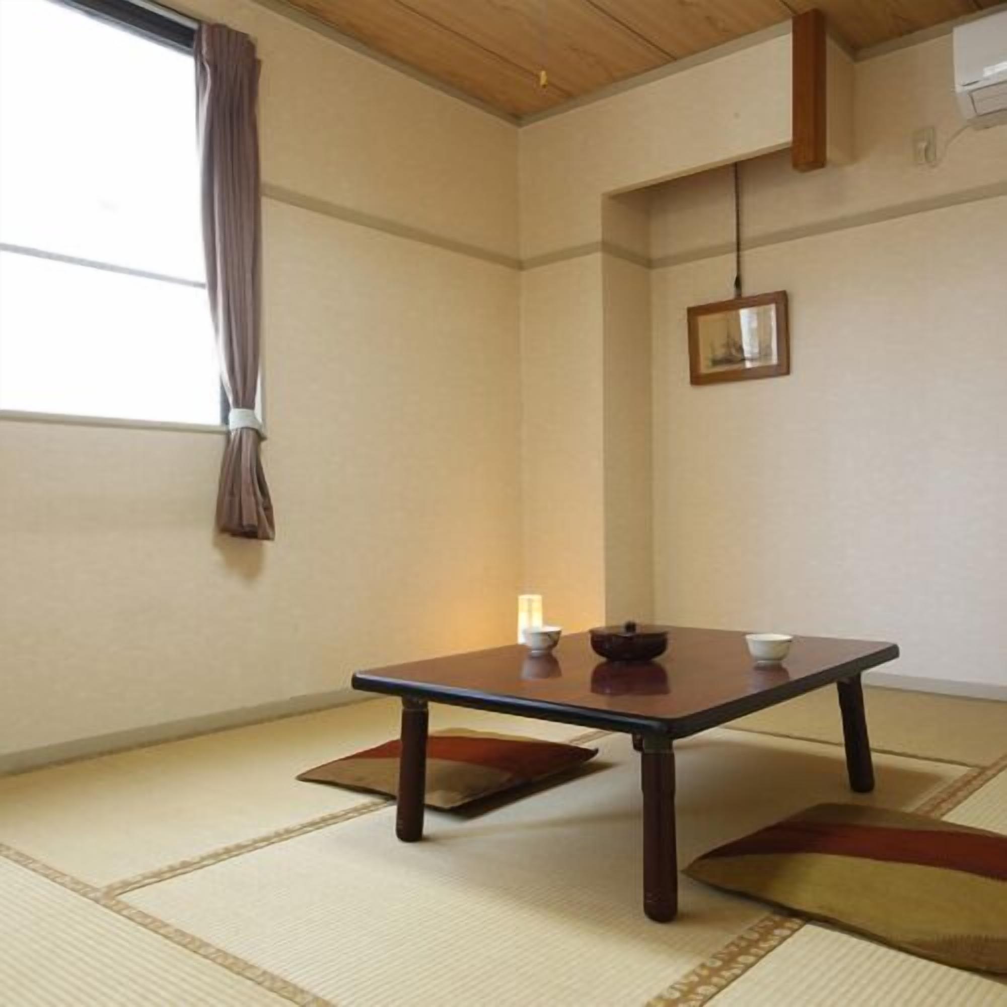 A traditional Japanese room with tatami flooring, a low table with a bowl and chopsticks, and a hanging picture frame.
