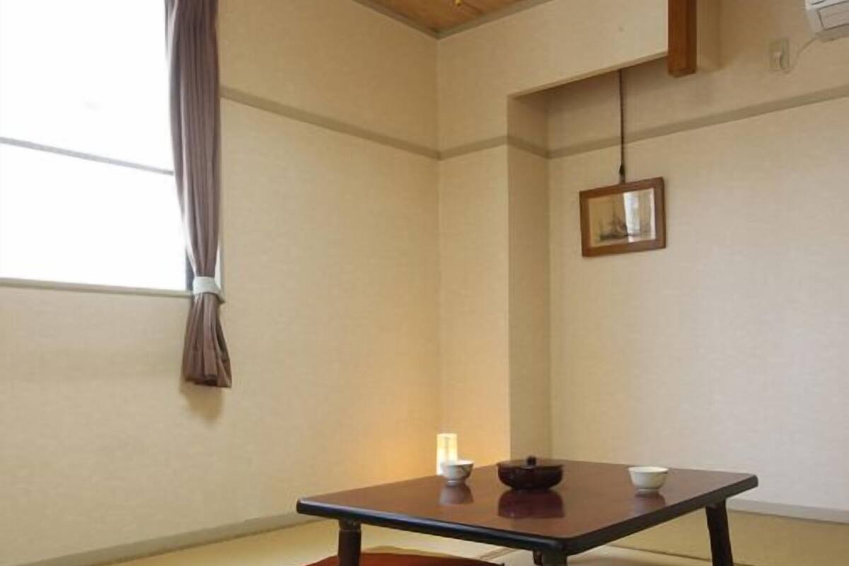 A traditional Japanese room with tatami flooring, a low table with a bowl and chopsticks, and a hanging picture frame.