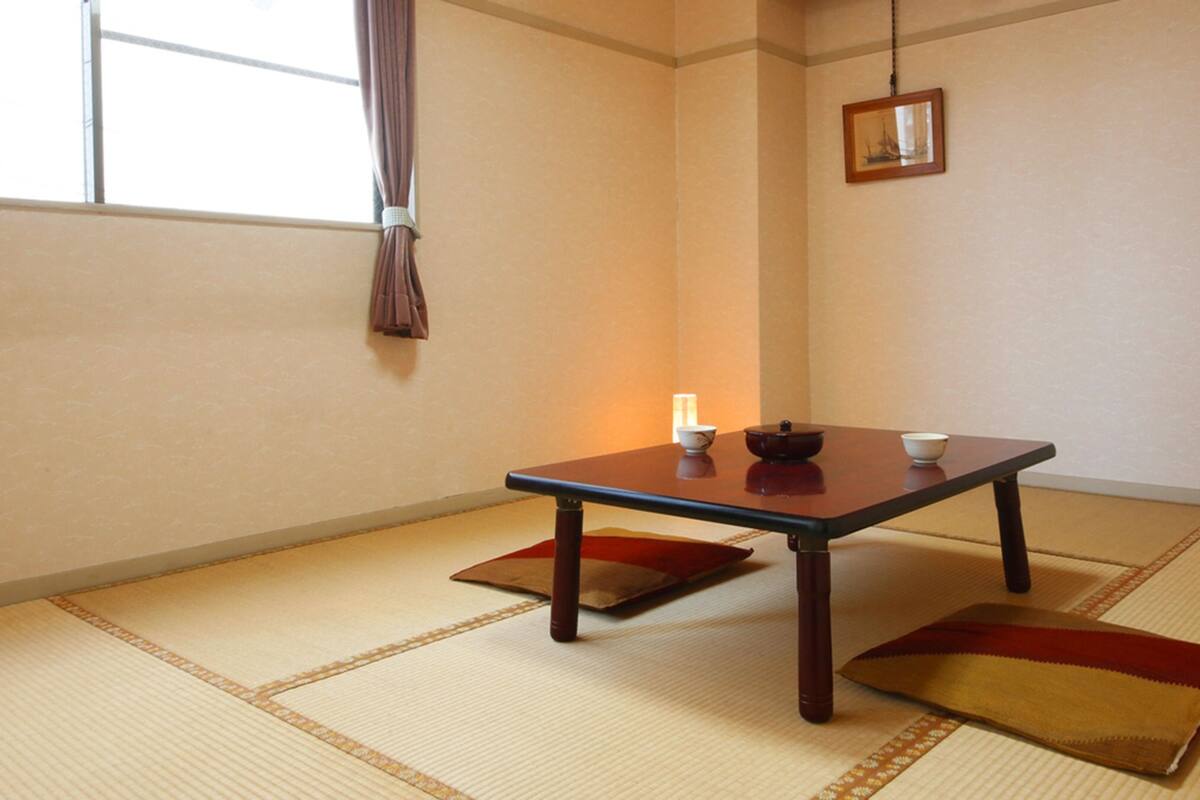 A traditional Japanese room with tatami flooring, a low table with a tea set, and a hanging picture frame.