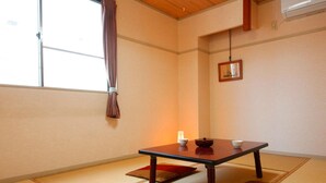 A traditional Japanese room with tatami flooring, a low table with a cushion, a hanging light, and a window with a curtain. - Kyomai Inn (Kyoto)