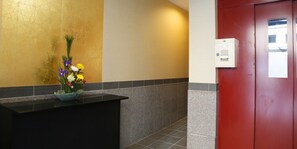 A reception area with a black counter, a flower arrangement, a red door, and a wall-mounted intercom. - Kyomai Inn (Kyoto)