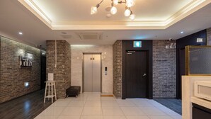 A modern lobby with a tiled floor, a reception desk, a black door, and a wall-mounted light fixture.