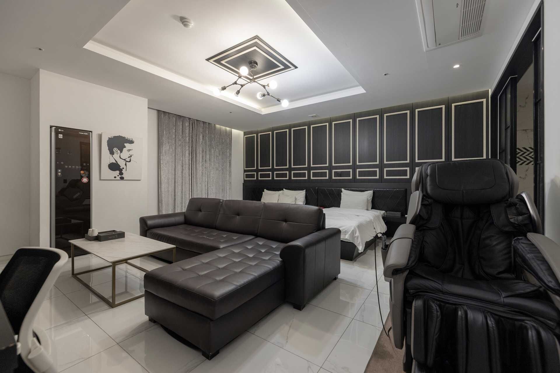 Una habitación de hotel moderna con un sofá grande, una cama, una silla de masaje y una mesa de centro de vidrio.
