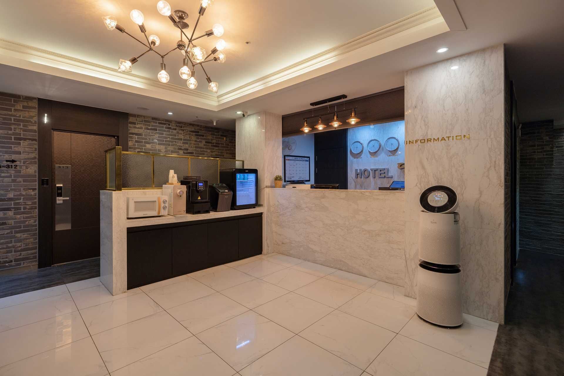 A hotel reception area with a modern design, featuring a reception desk, a digital screen, a clock, and a trash bin.