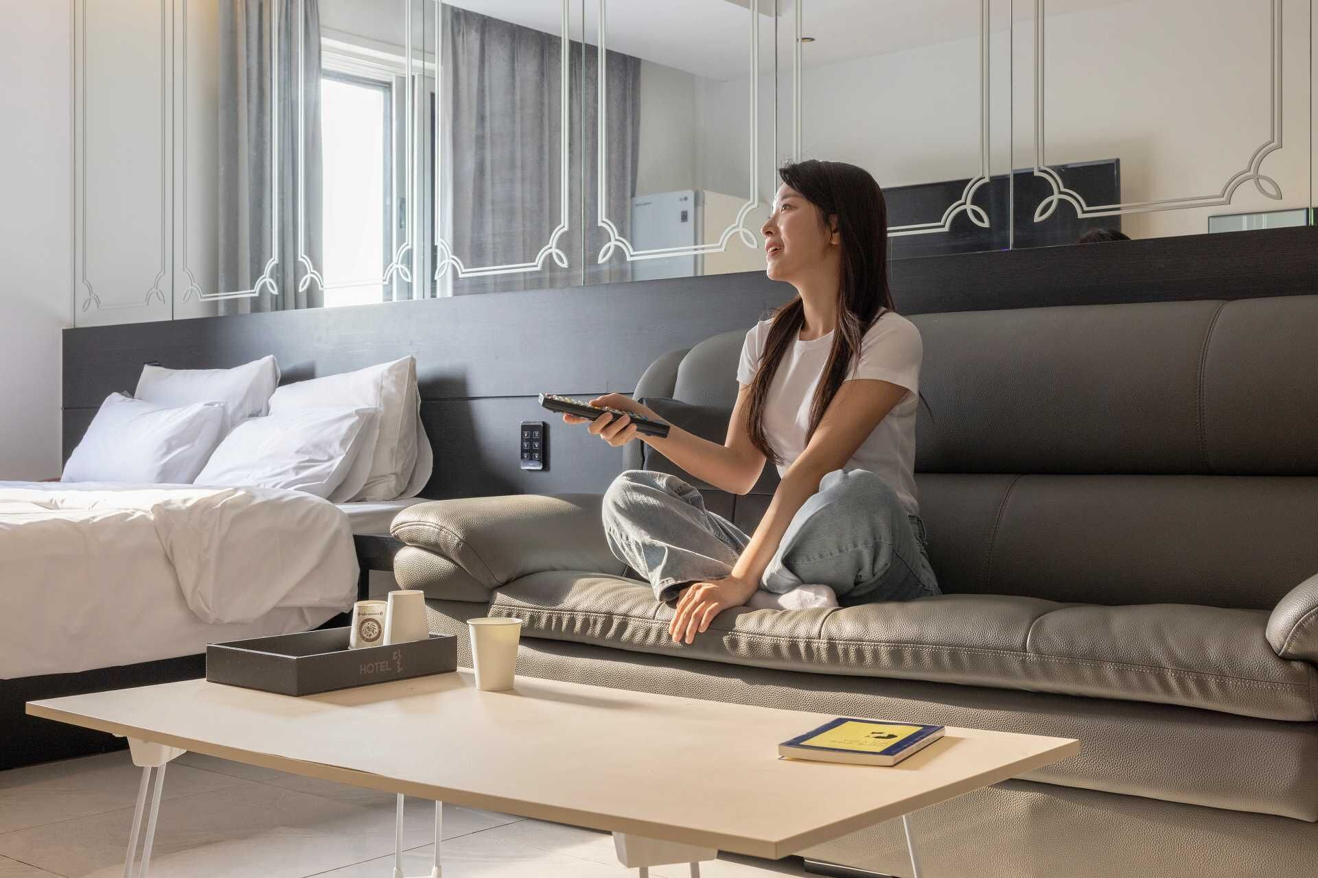 A modern hotel room with a sofa, a bed, a coffee table, and a remote control.