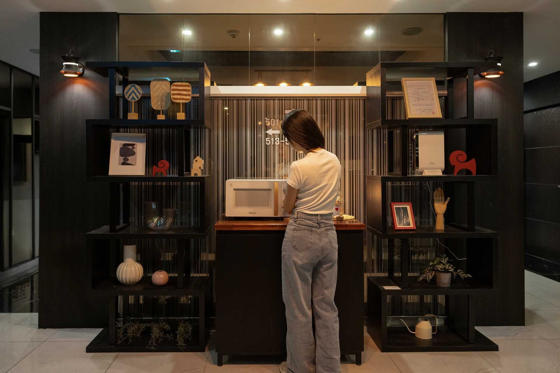 Un intérieur moderne avec un bureau central, entouré d’étagères en bois foncé où sont disposés divers objets décoratifs et un four à micro-ondes.