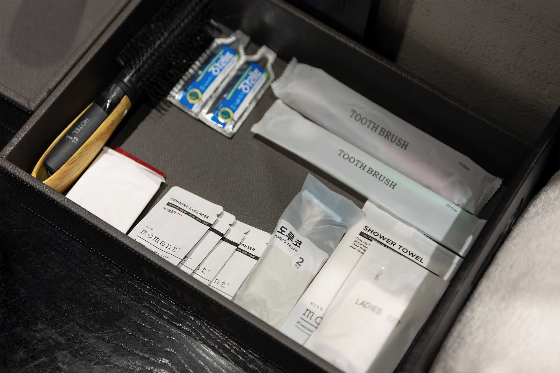 A neatly organized toiletry bag containing items like a toothbrush, toothpaste, a toothbrush brush, a shower towel, and feminine hygiene products.