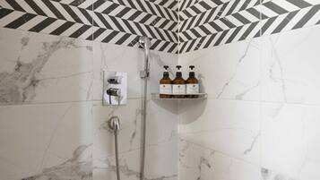 A bathroom with a shower, a hand dryer, and a shelf with three bottles of shampoo and conditioner.