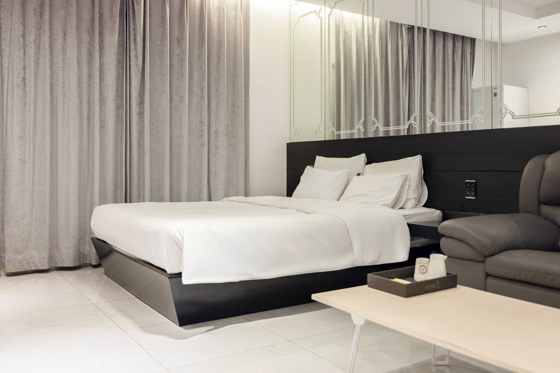 Una habitación de hotel moderna con una cama grande, un sofá, una mesita y un espejo.