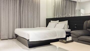 Una habitación de hotel moderna con una cama grande, un sofá, una mesita y un espejo.