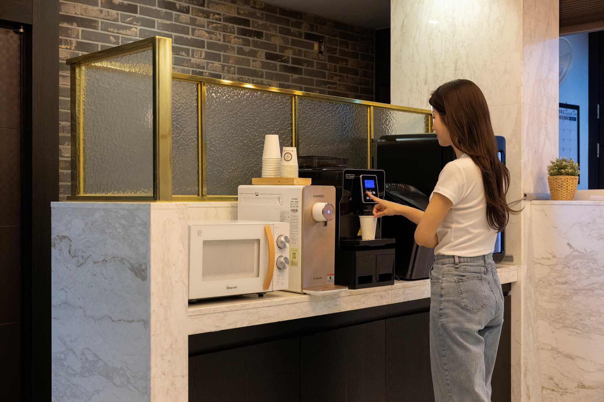 A coffee machine with a digital display, a microwave, and a stack of disposable cups on a marble countertop.