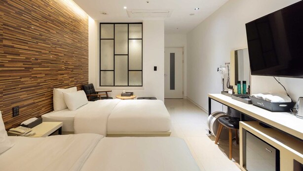 A modern hotel room with a large bed, a desk with a flat-screen TV, and a wooden accent wall.