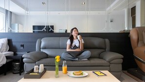 A modern hotel room with a grey sofa, a white table with breakfast items, and a TV in the background.