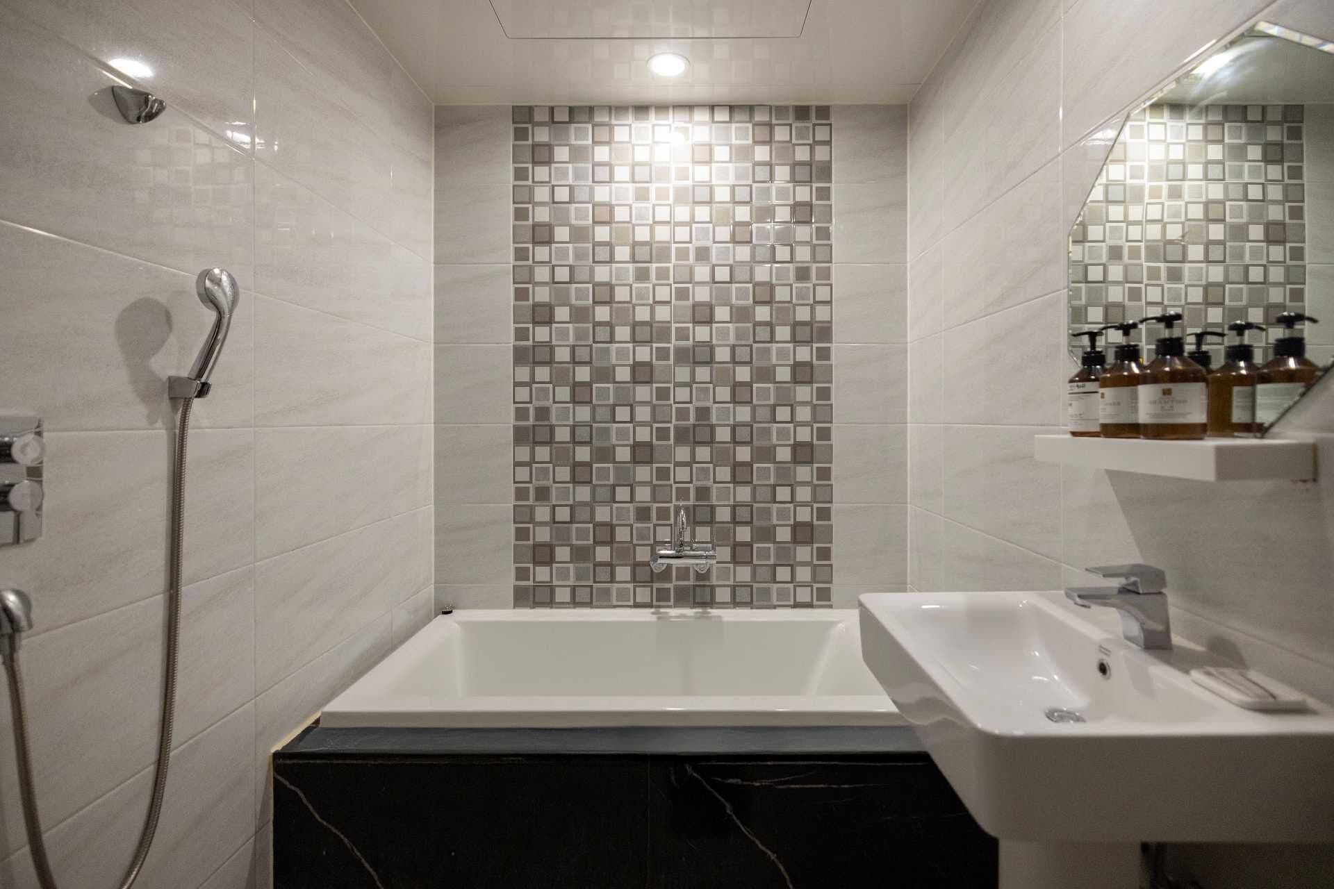 Un bany modern amb una banyera blanca, una dutxa amb un braç de dutxa manual i un lavabo amb un mirall a sobre.