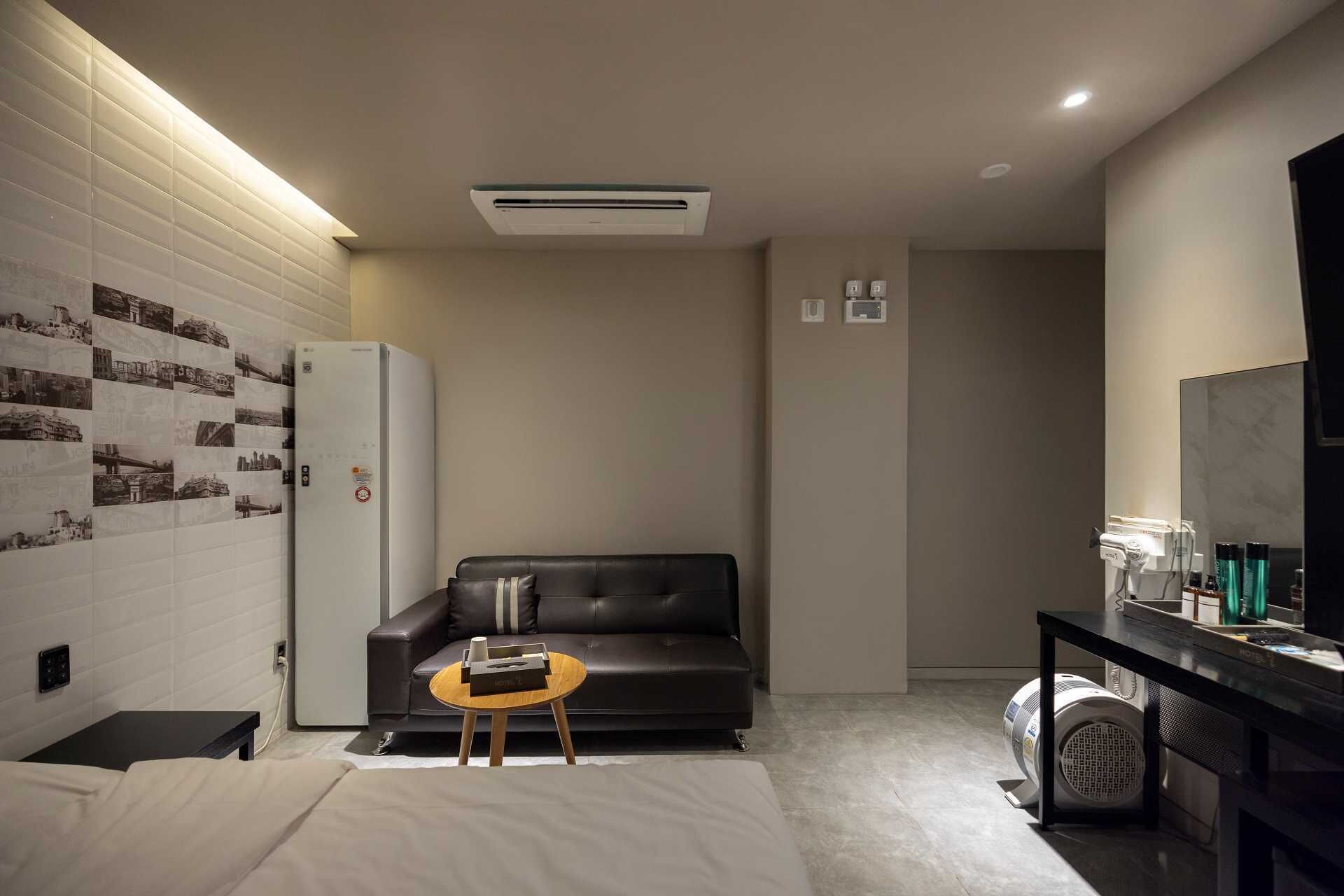 Habitación de hotel con cama, sofá, mesita, televisión y aire acondicionado instalado en la pared.