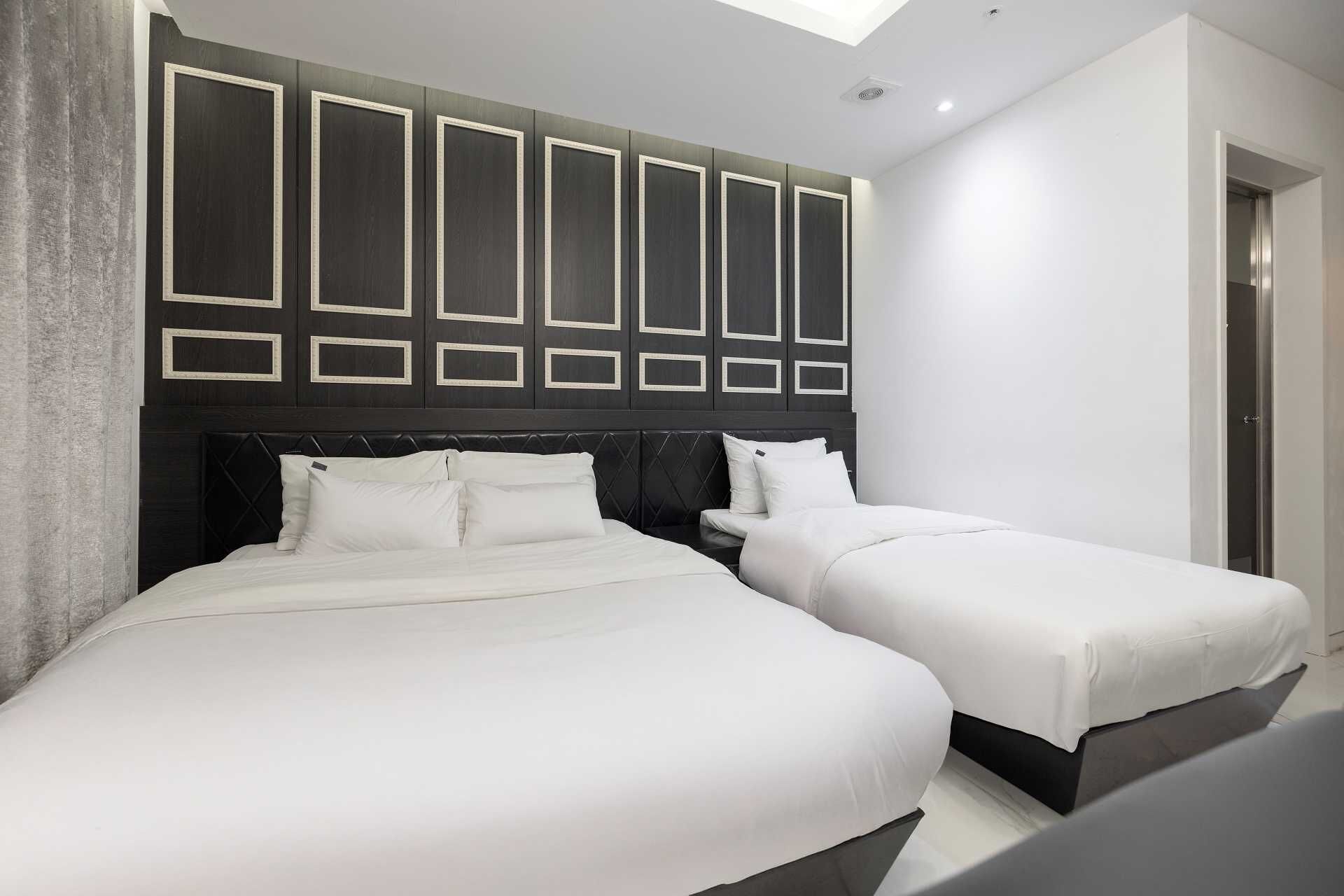 Una habitación de hotel moderna con dos camas, un cabecero oscuro con diseños geométricos y un tragaluz arriba.