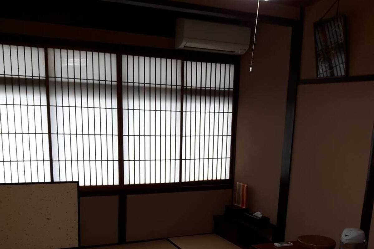 A tatami mat room with a sliding door, a heater, a small table with a kettle, and a shelf with decorative items.