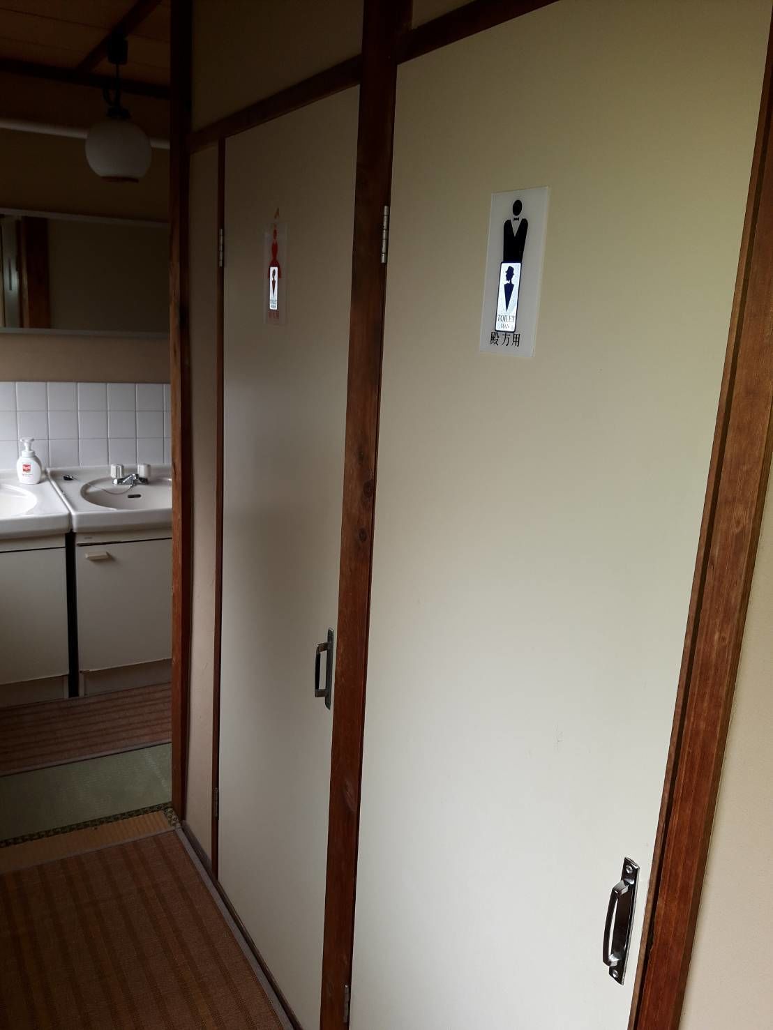 A bathroom with a sink, mirror, and toilet stalls.