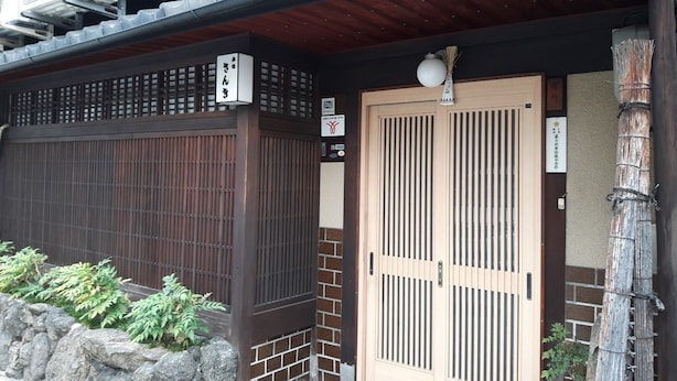 Un edificio japonés tradicional con una puerta de madera, un muro de piedra y un pequeño jardín.