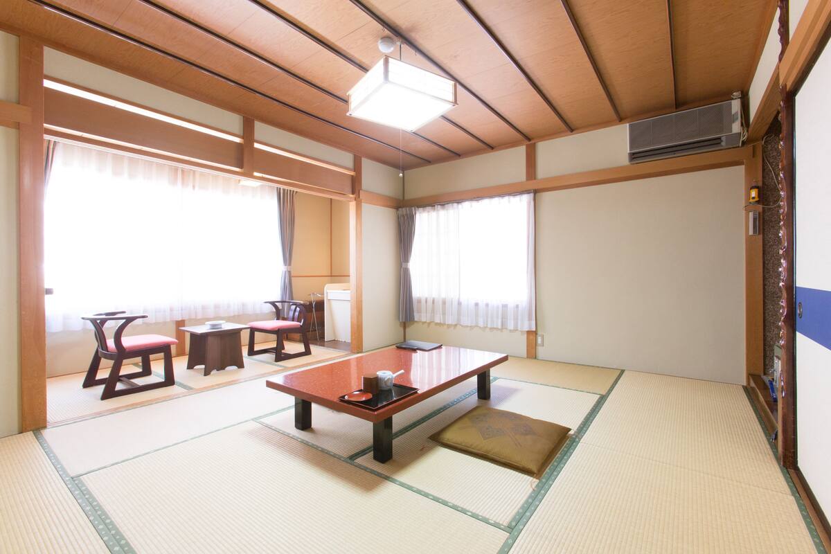 Una habitación japonesa tradicional con suelo de tatami, una mesa baja, sillas y puertas correderas.