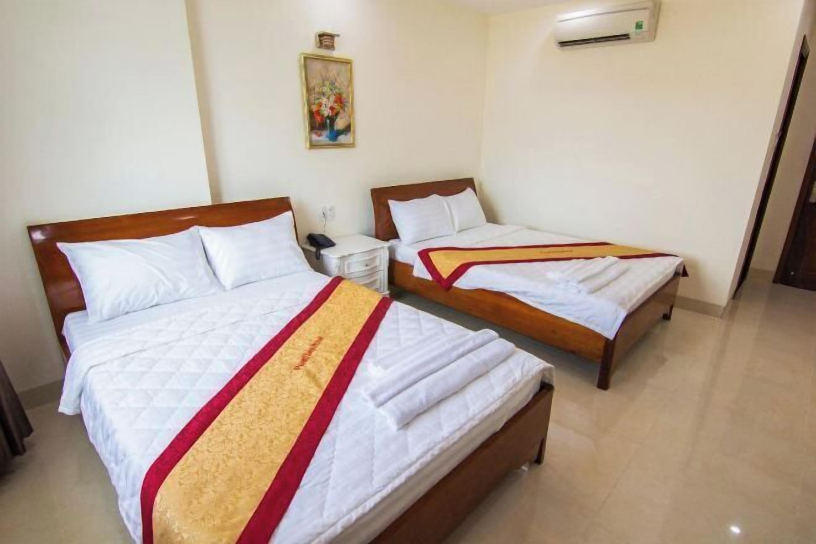 Een hotelkamer met twee bedden, een nachtkastje met telefoon, een wandairconditioner en een schilderij aan de muur.