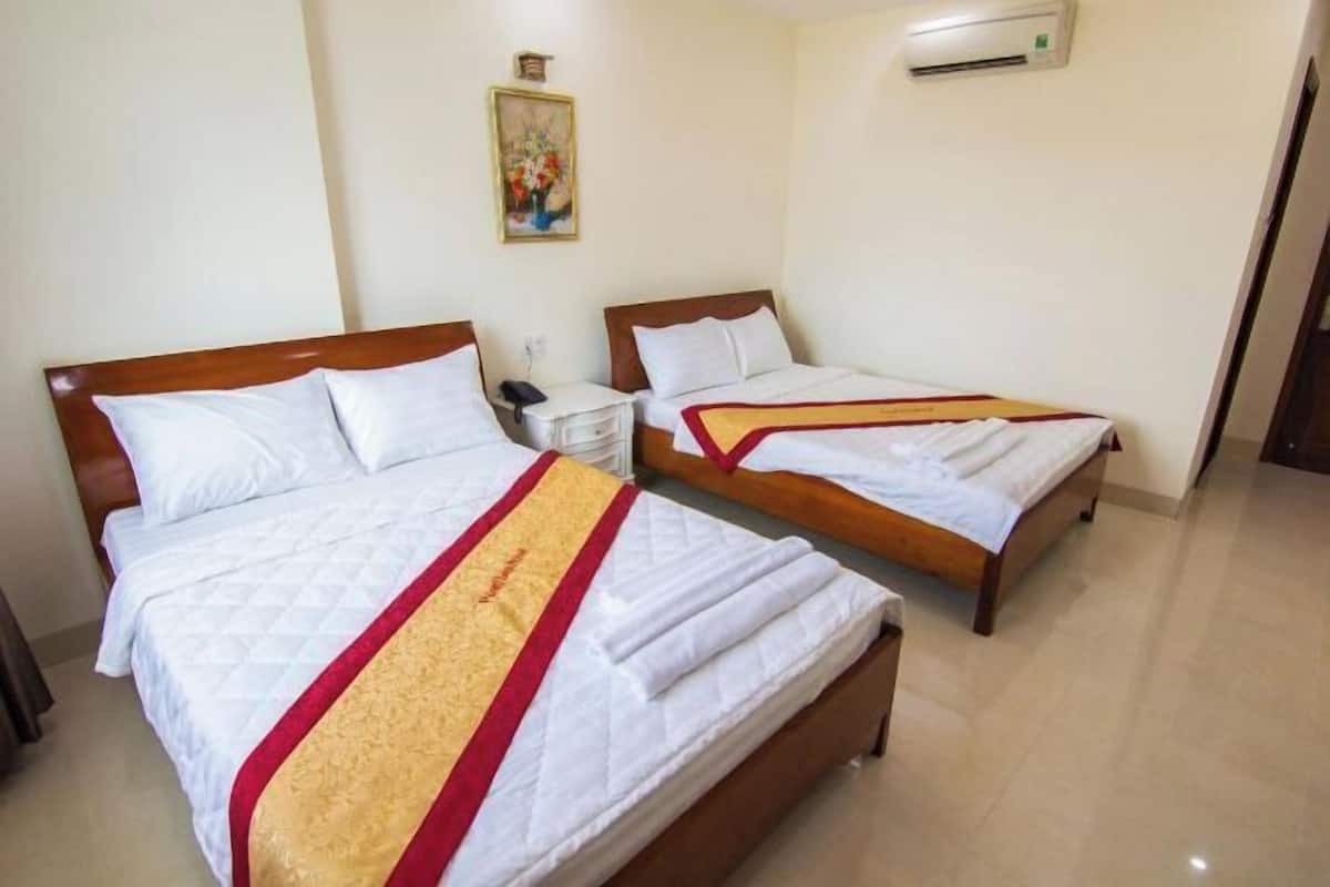 Quarto de hotel com duas camas, uma mesinha de cabeceira com telefone, ar-condicionado na parede e um quadro na parede.