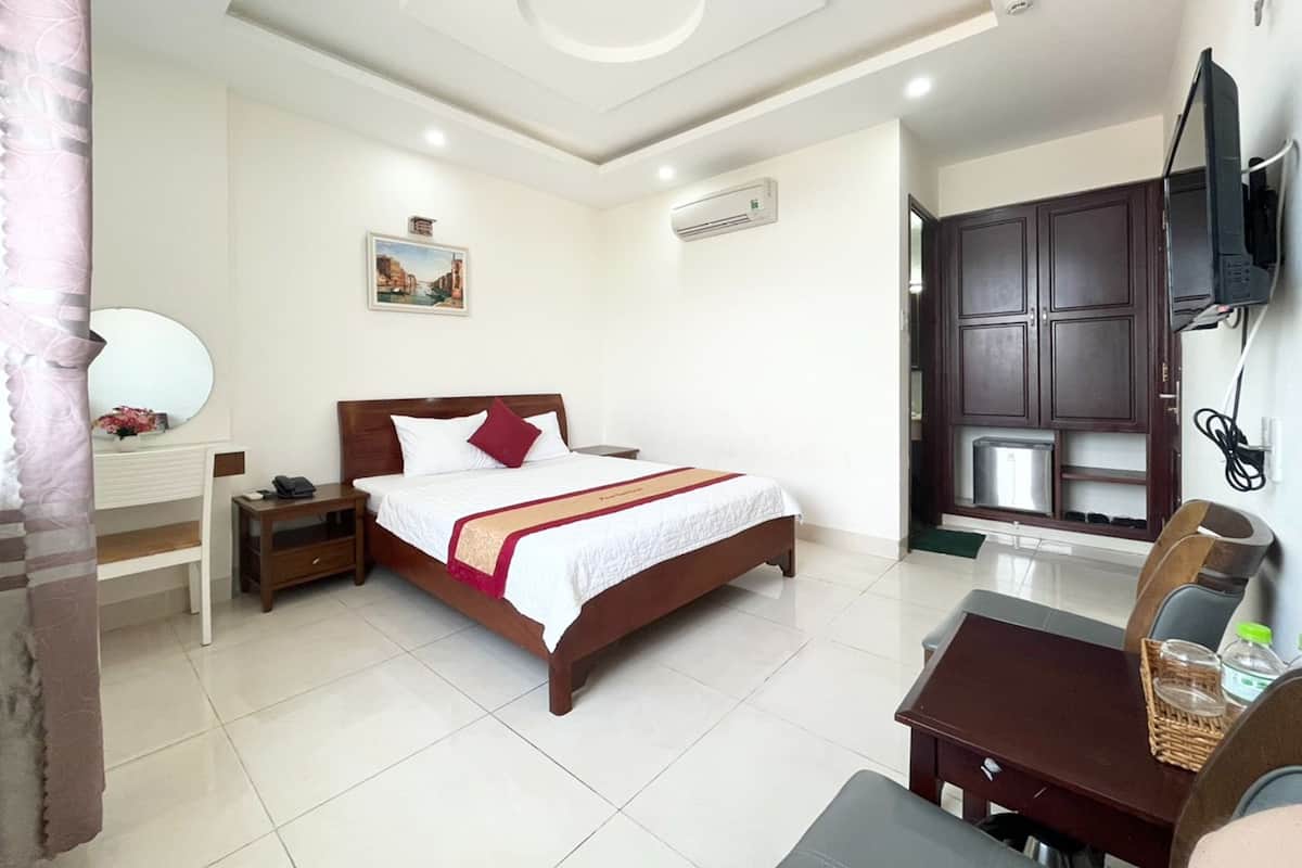 Quarto de hotel com cama, mesa de cabeceira, escrivaninha com cadeira, televisão na parede e um armário grande.