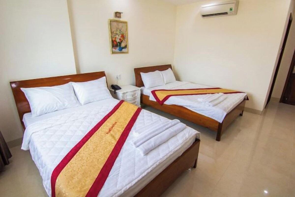 Habitación de hotel con dos camas, una mesita de noche con teléfono, aire acondicionado en la pared y un cuadro colgado.