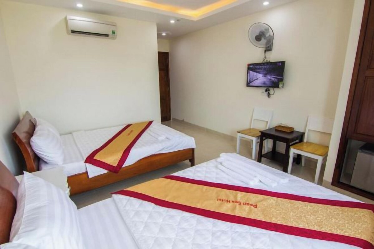Een hotelkamer met twee bedden, een televisie, een ventilator en een klein tafeltje met stoelen.