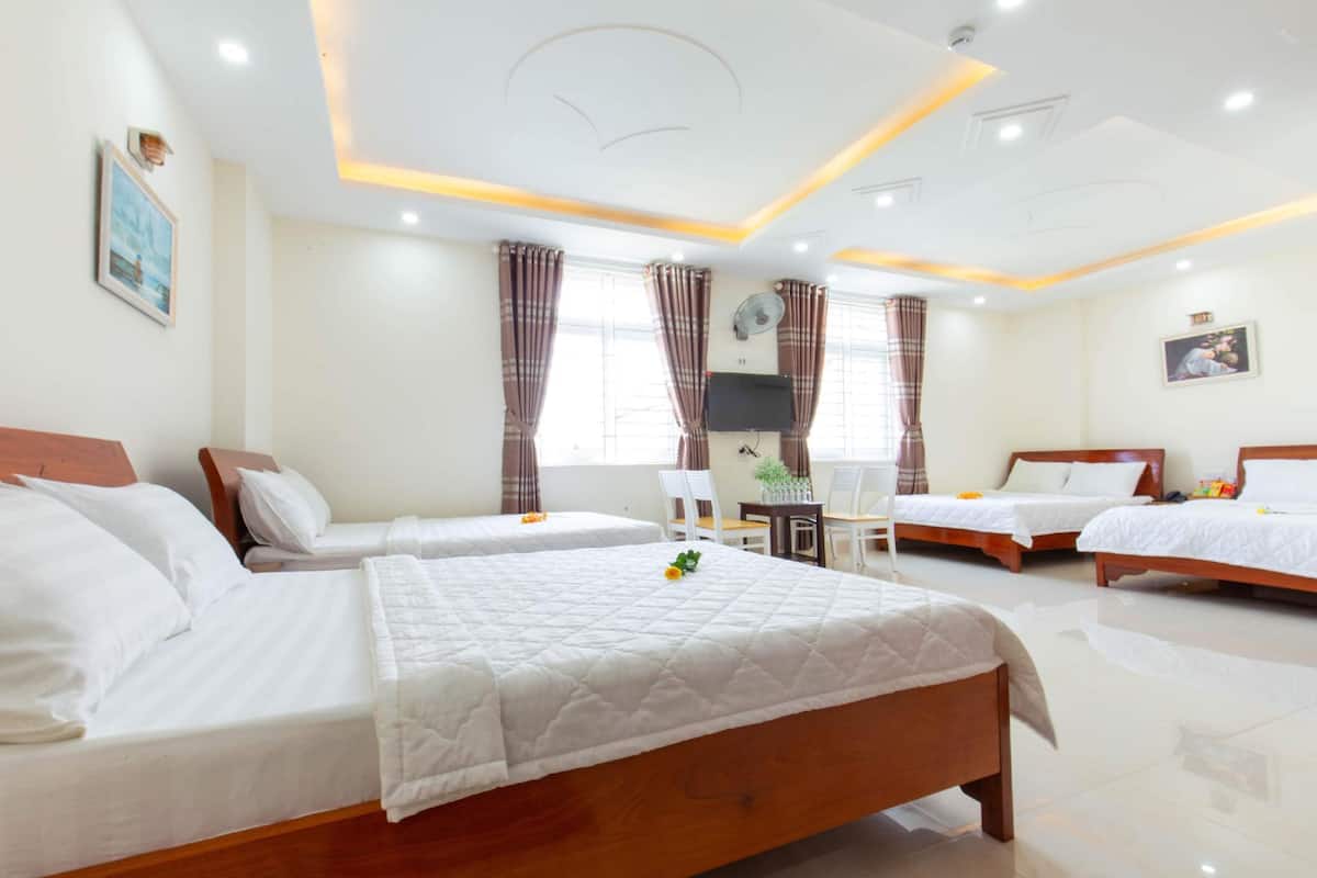 Quarto de hotel com três camas, uma escrivaninha e uma cadeira.