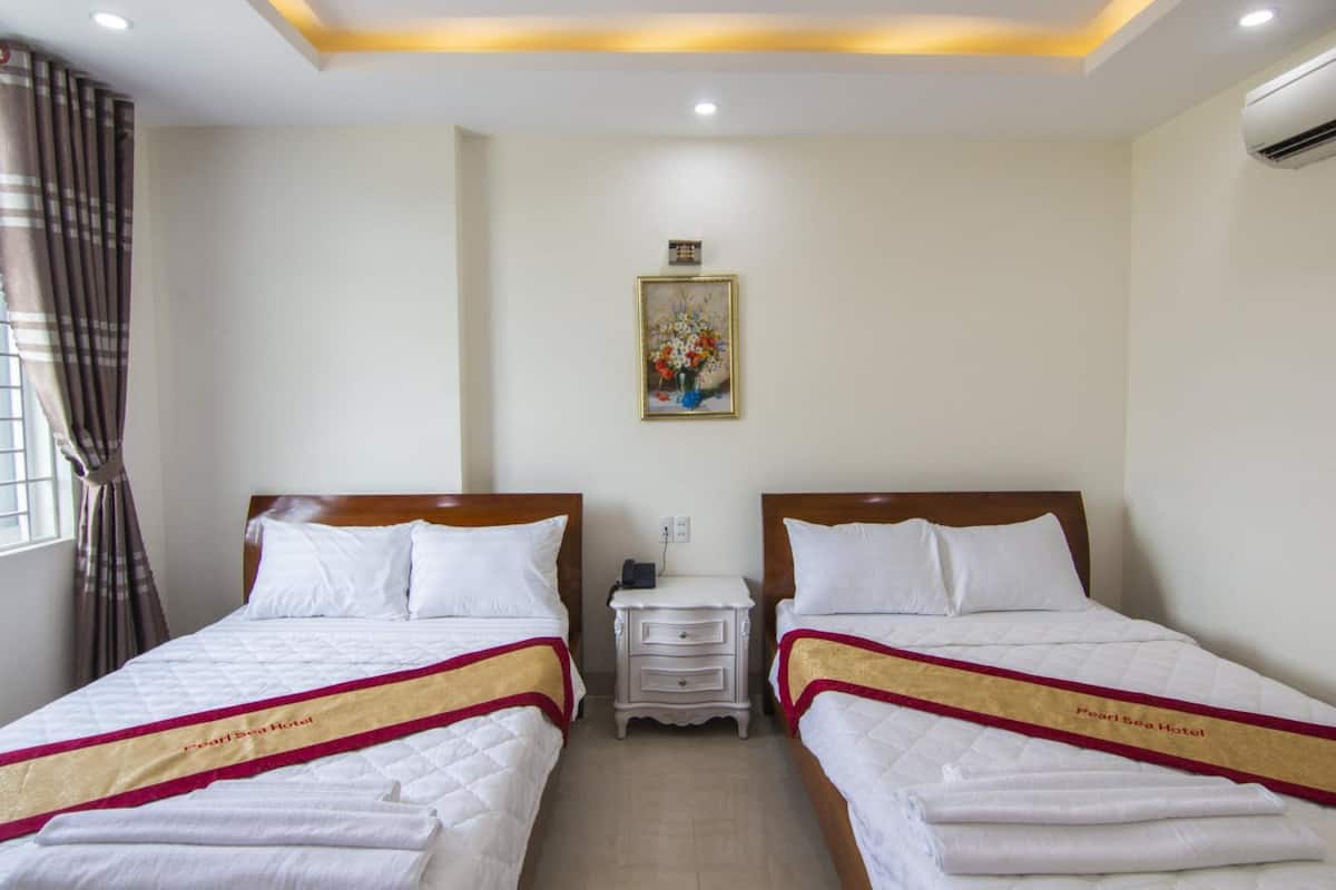 Quarto de hotel com duas camas, uma mesa de cabeceira, um quadro na parede e uma janela com cortinas.