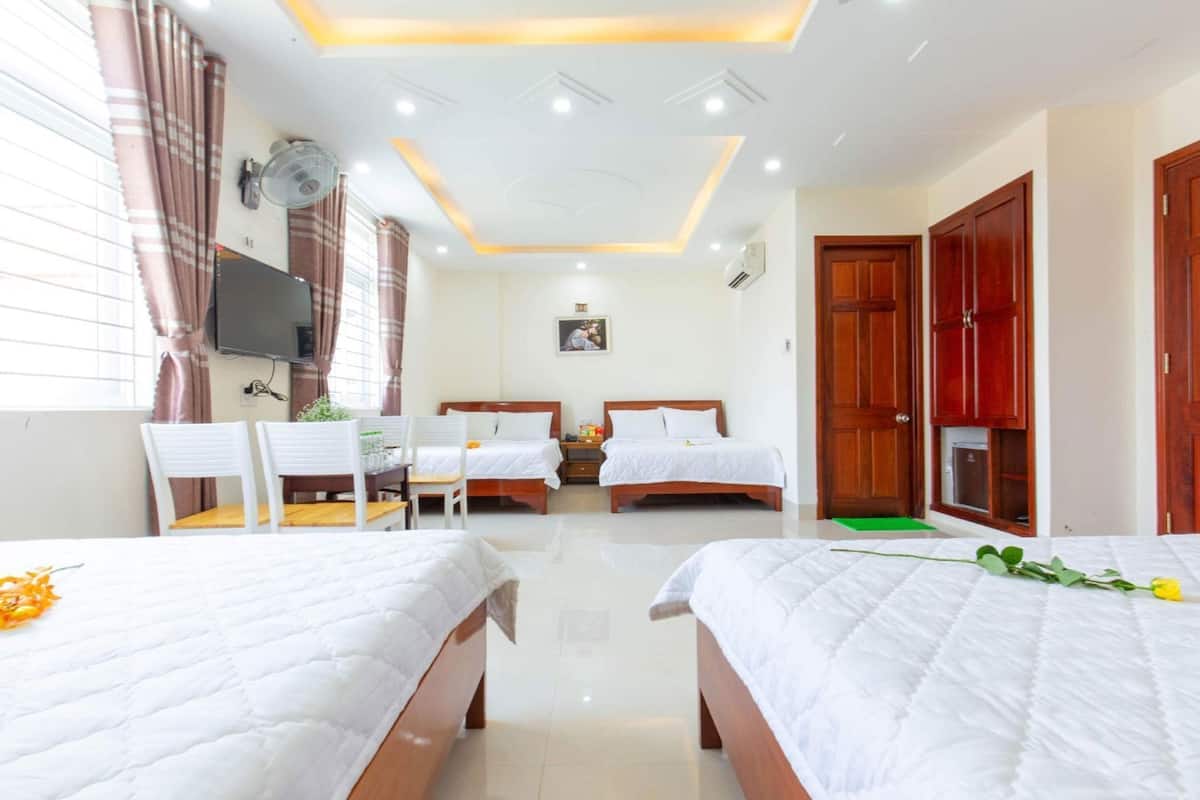 A hotel room with two beds, a dining table with chairs, a TV, and a ceiling fan.