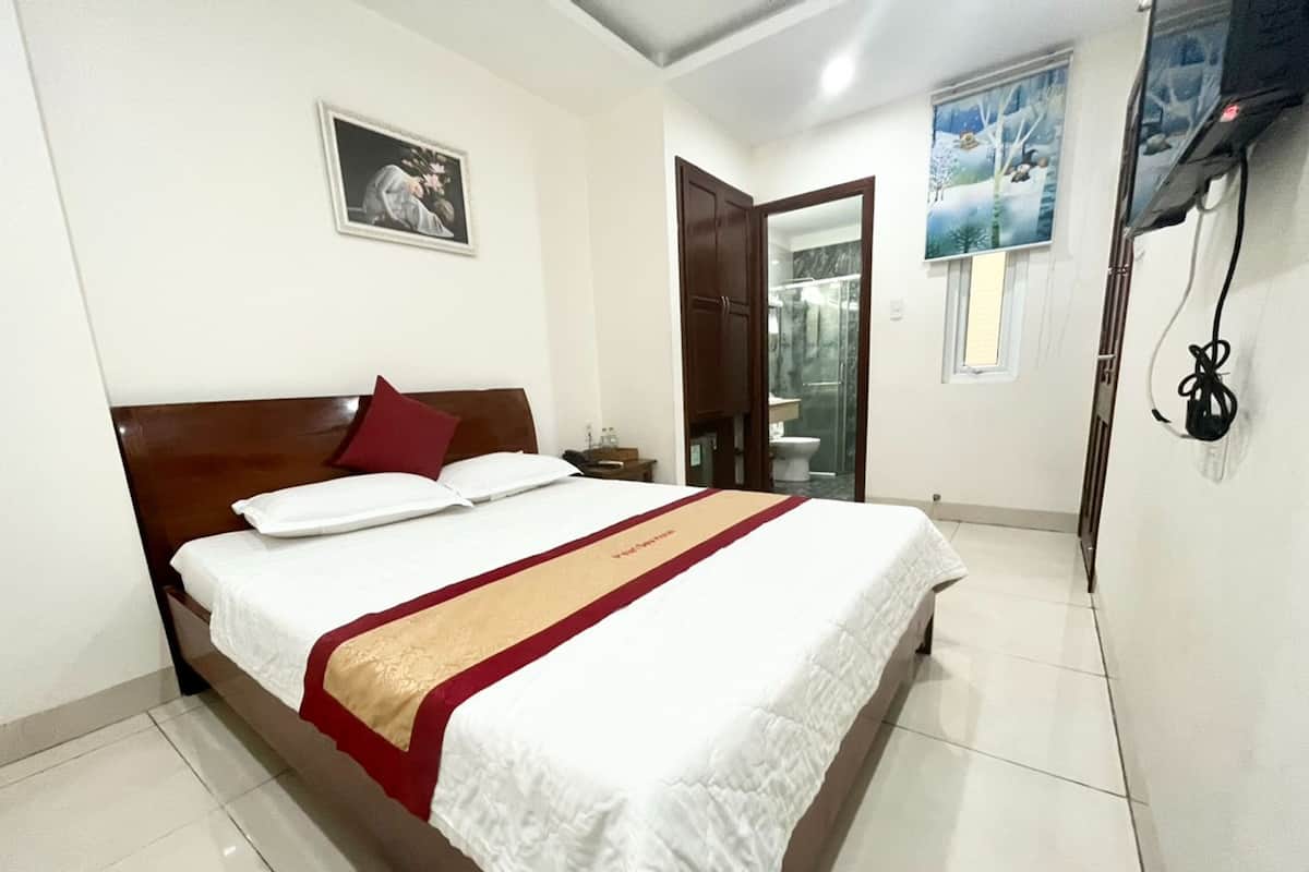 Quarto de hotel com cama, mesa de cabeceira, quadro na parede e banheiro visível por uma porta aberta.
